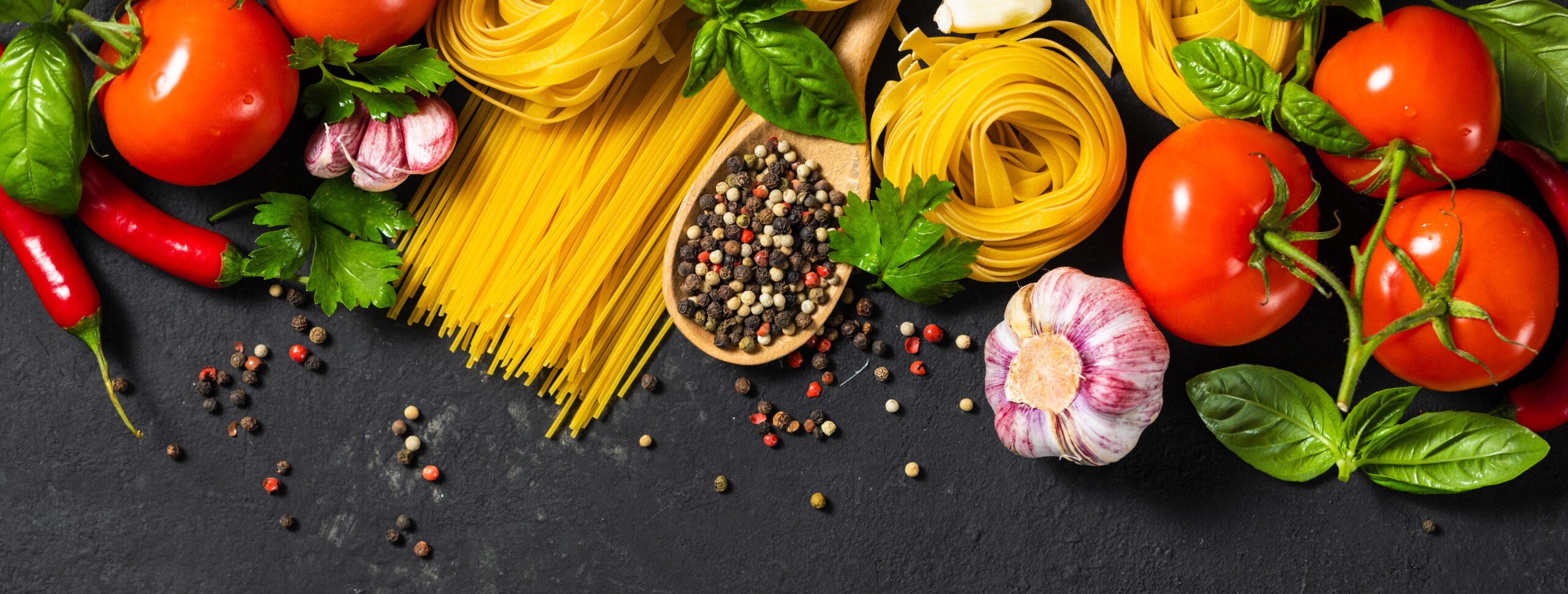 Italian food ingredients with pasta, tomatoes, pepper, garlic and parsley on dark background with copy space, top view